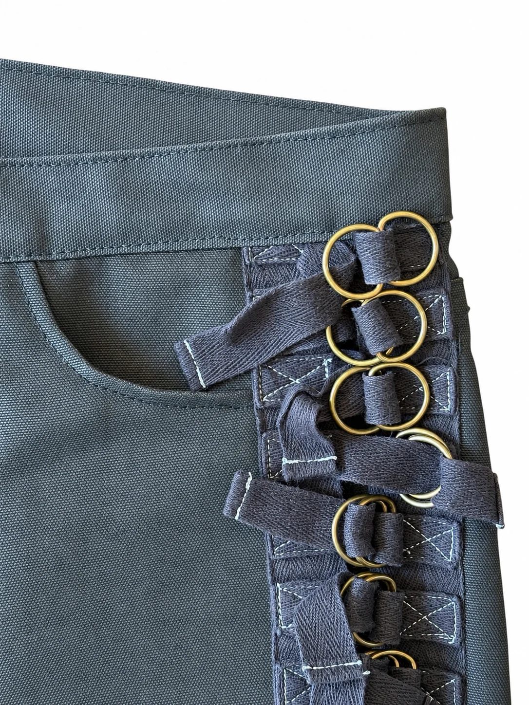 Close-up of black waxed denim, cotton bondage straps, and brass rings.