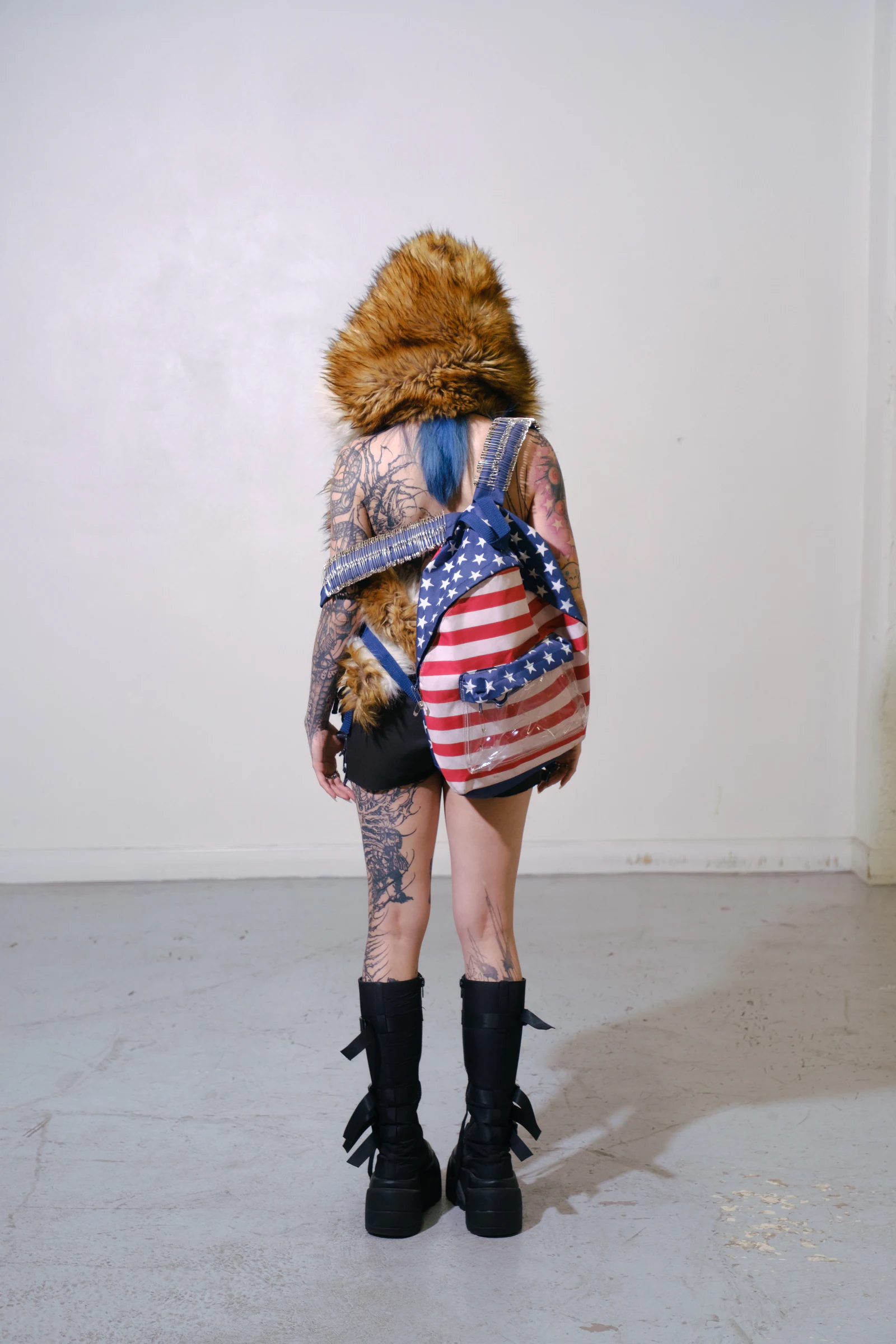 Back view of a tattooed model wearing the Armor Backpack — American Flag in a studio.